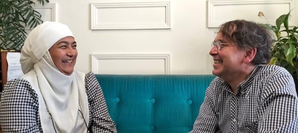 A woman and a man seated on a blue couch haveing a conversation.